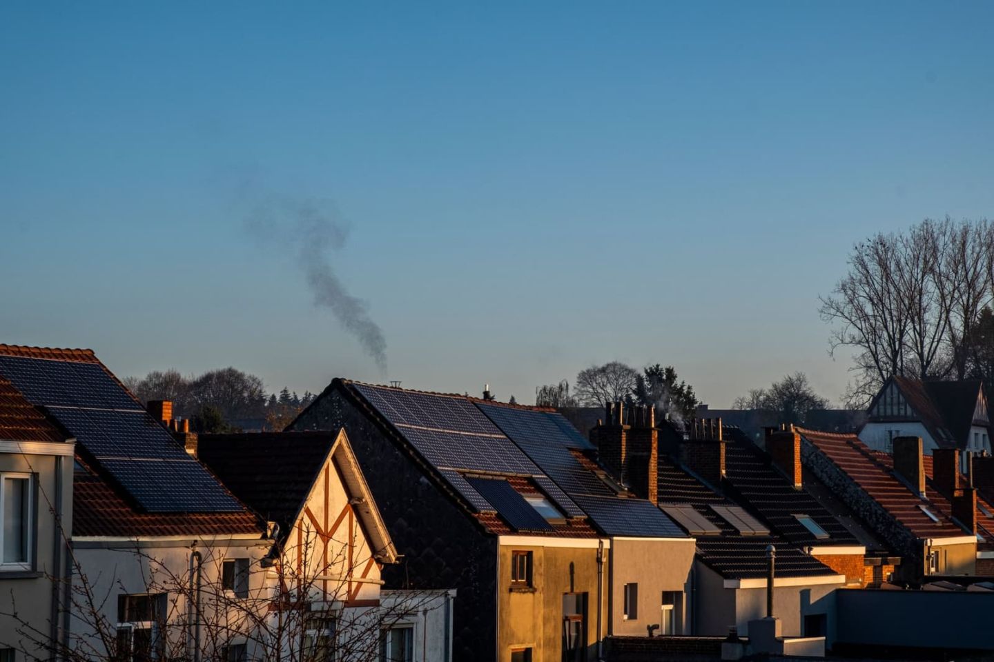 Reihe von Wohnhäusern mit Photovoltaikmodulen auf den Dächern, aufgenommen von einem erhöhten Standpunkt im Abendlicht.