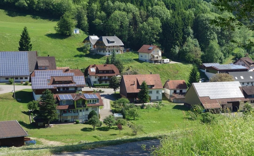 Erhöhter Blick über eine Ortslage, auf mehreren Wohnhäusern und Wirtschaftsgebäuden liegen Photovoltaikmodule.